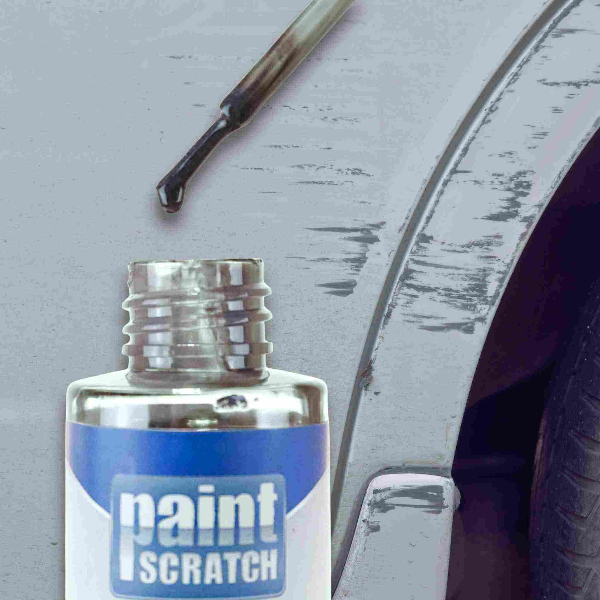Close-up of a PaintScratch touch up bottle with brush applicator held near a scratched car fender, showing how the paint is applied to damaged areas.
